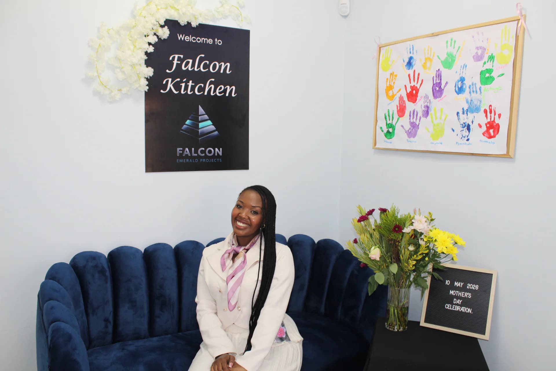 Falcon Kitchen team member seated near flowers and branded wall signage